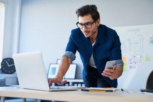 Developer at desk looking at laptop and holding a phone simultaneously