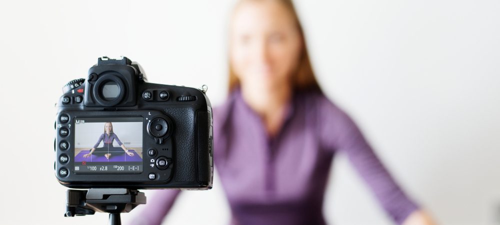 A social influencer in front of a camera resting on tripod getting ready to record