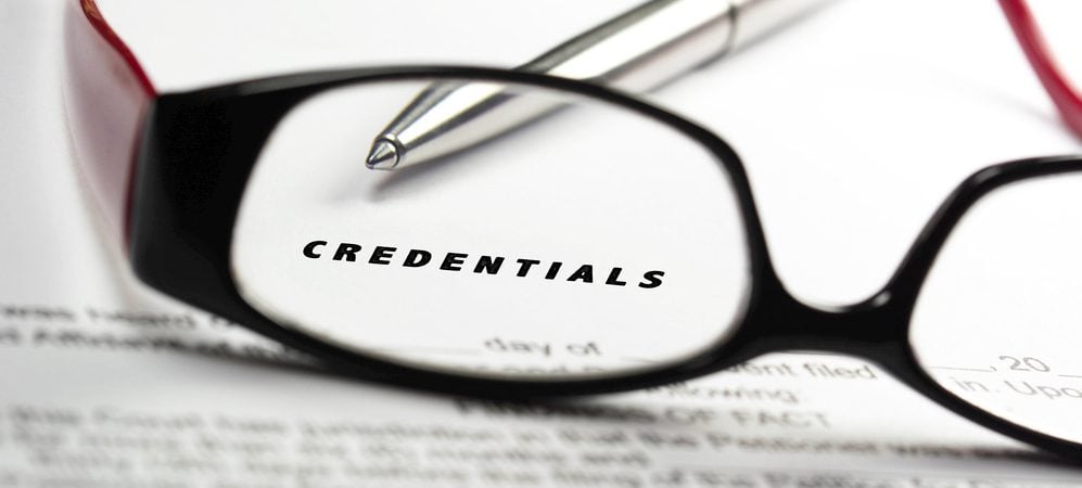 The word "Credentials" written on fine print being examined under dark rimmed glasses