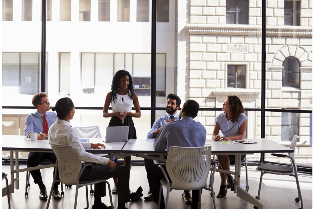 Young woman presenting in front of her coworkers gathered around a conference table