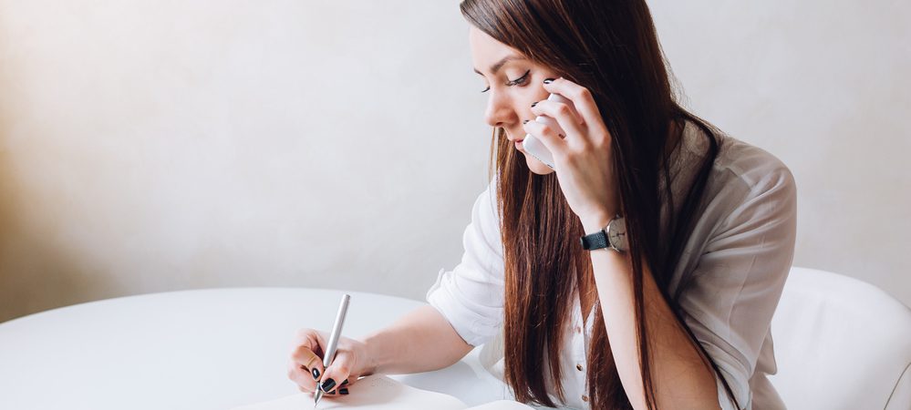 Young woman cold calling and taking notes