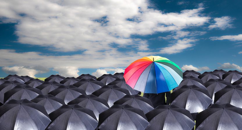 A series of umbrellas with one multi-colored one standing amongst them.