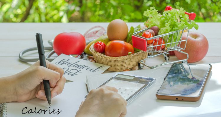 Woman tracking calories with vegetables and a phone in the background