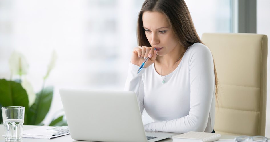 A woman thinking while looking at a laptop screen.