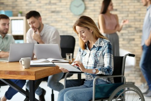 Young woman in wheelchair and colleagues at workplace