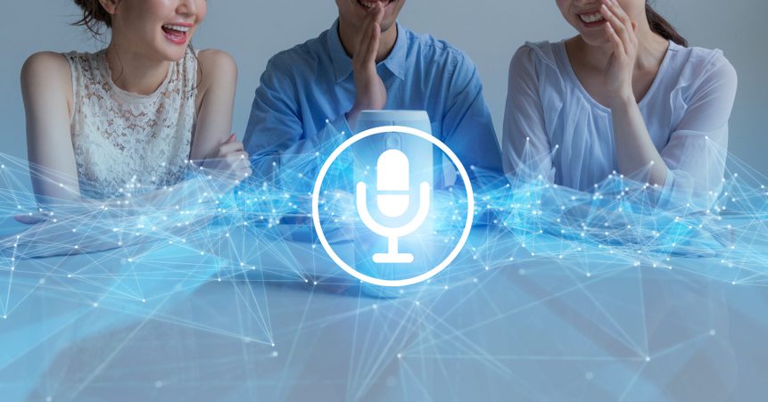 Three coworkers sitting at a table and having a great time chatting with a smart speaker