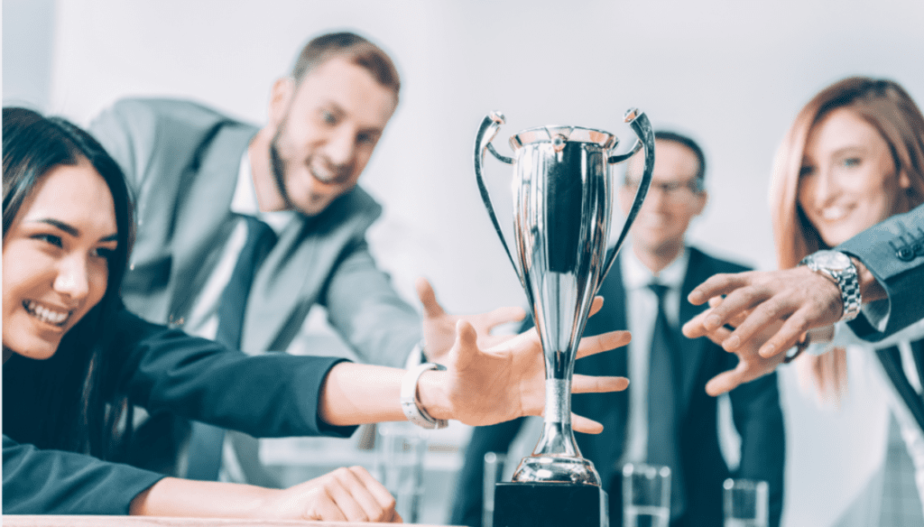 Group of people reaching for a trophy.