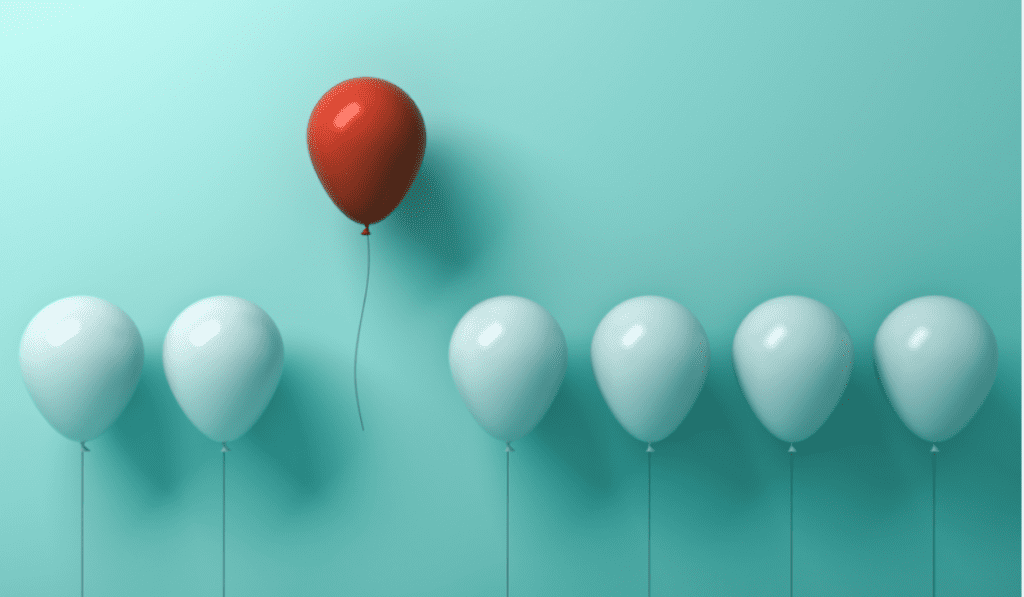 A series of white balloons with one red balloon floating above the rest.