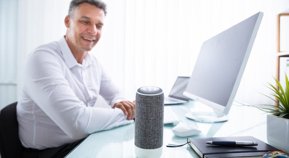 Man sitting in front of his computer and talking to his smart speaker