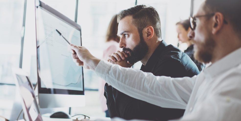 Man pointing with a pen at a monitor, while his coworker is paying attention