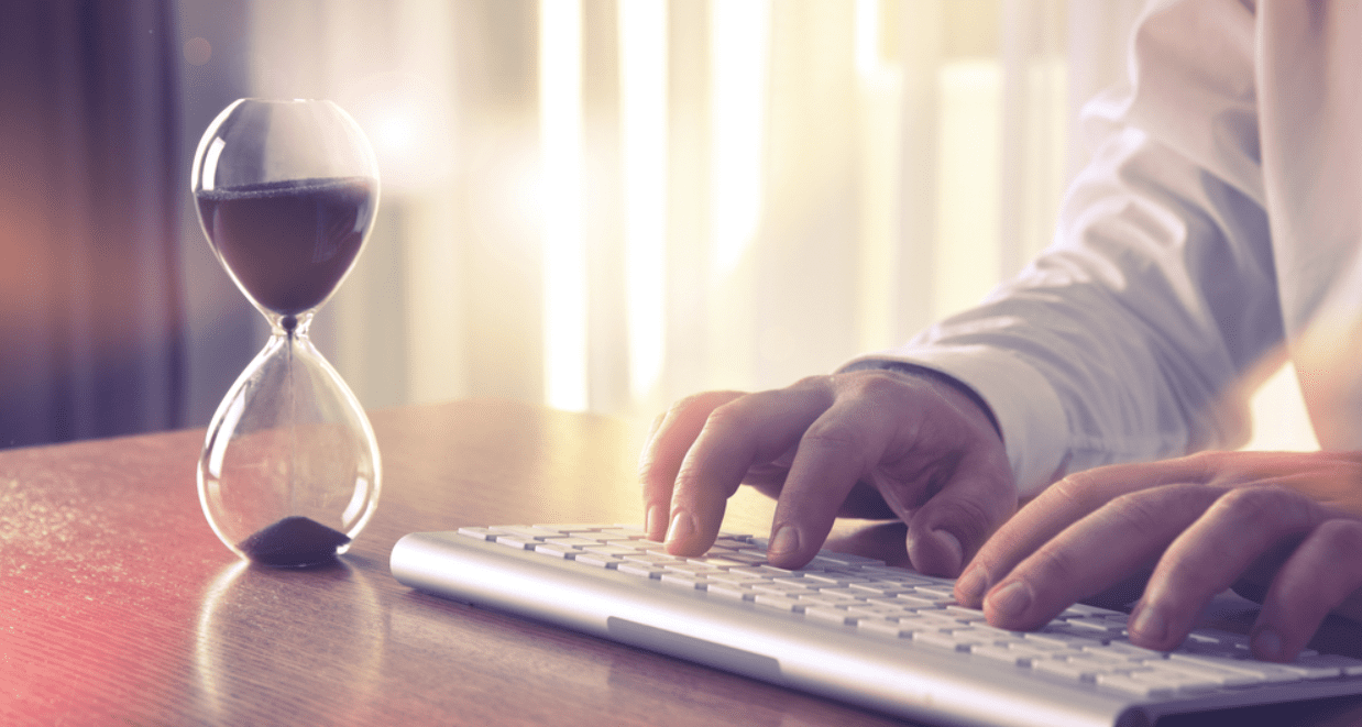 Man typing at a keyboard with an hourglass next to him.