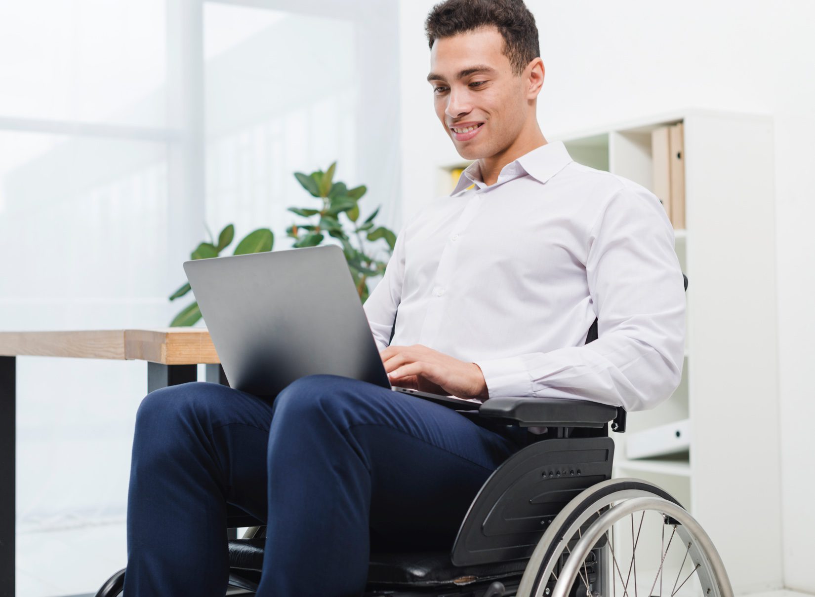 Man in a wheelchair looking at laptop on his lap and smiling.