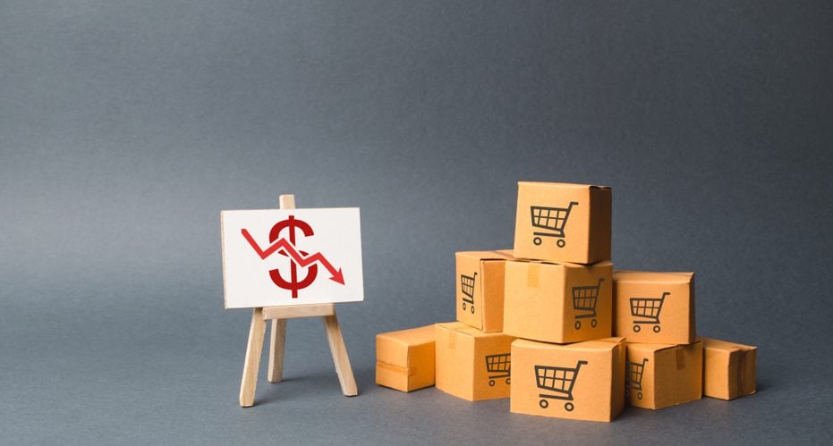 Stacks of boxes with shopping cart drawn on them sitting next to a canvas stand board with a dollar sign on it. 