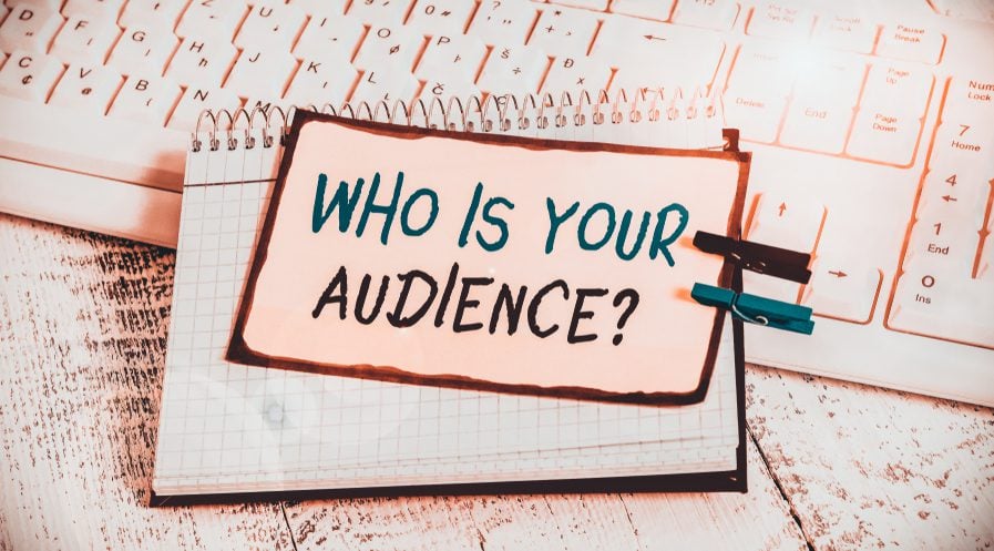 Sign that reads "Who is your audience" clipped with wooden clothespins to a notebook