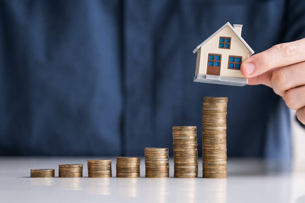 real estate marketing Close-up Of Businessman Hand Arranging House Model On Stacked Coins At Desk