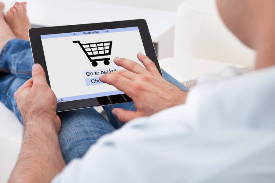 A man sits down and clicks on a shopping cart on a tablet