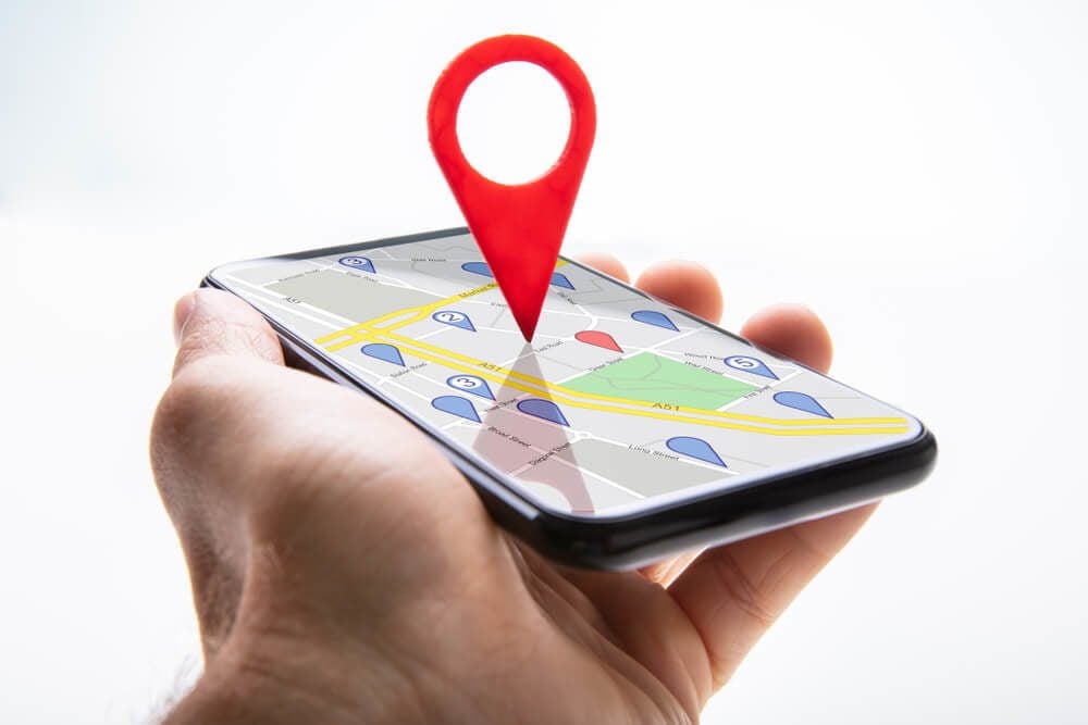 local search_Close-up Of A Person's Hand Holding Cellphone With Red Map Pin Pointer Against White Background