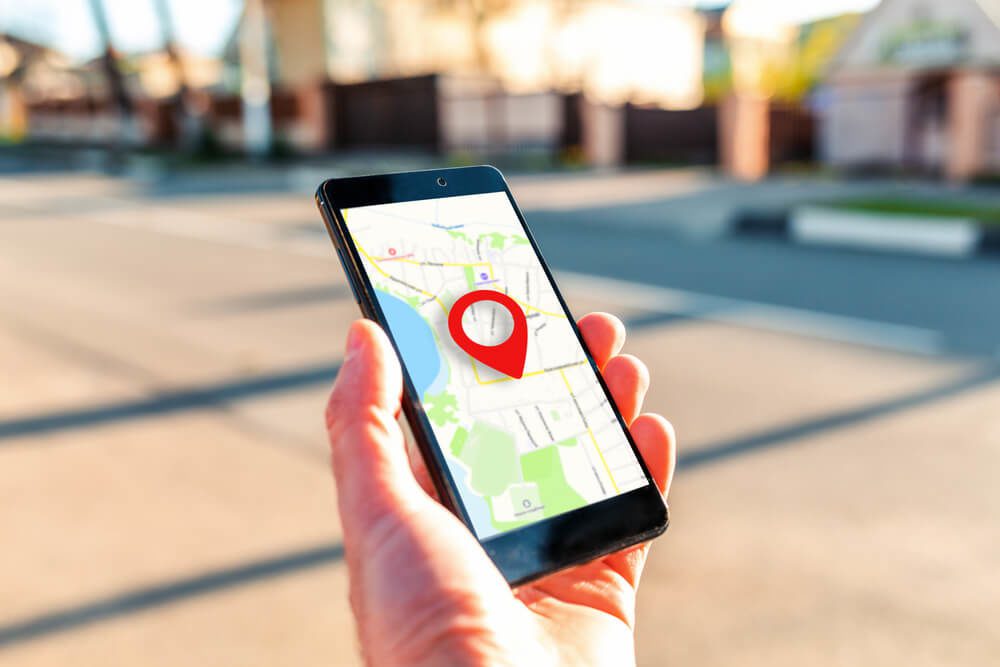 local search_Male hand holding holding smartphone with online-a map on which the geolocation icon. In the background, a blurred street. Close up. Concept of online navigation and GPS