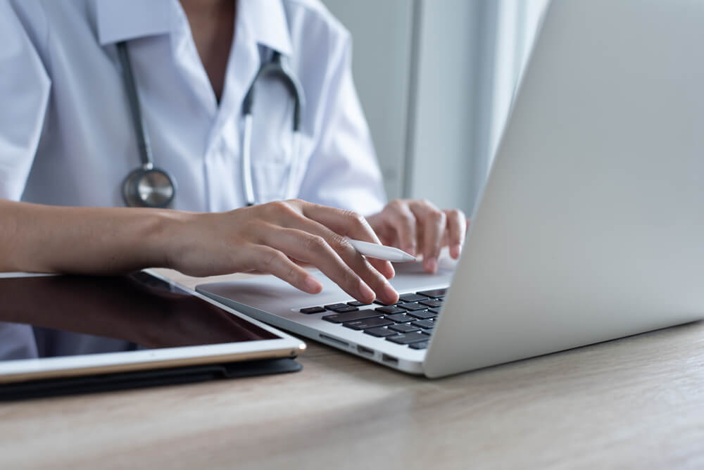 medical search_Female doctor working on laptop computer and using digital tablet in medical office, close up. Medical online, Ehealth, telemedicine concept