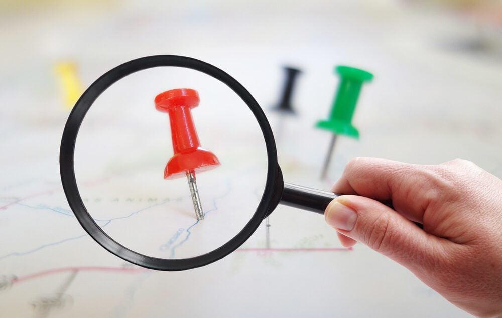 local search_Magnifying glass looking at closeup of push pin tacks in a map