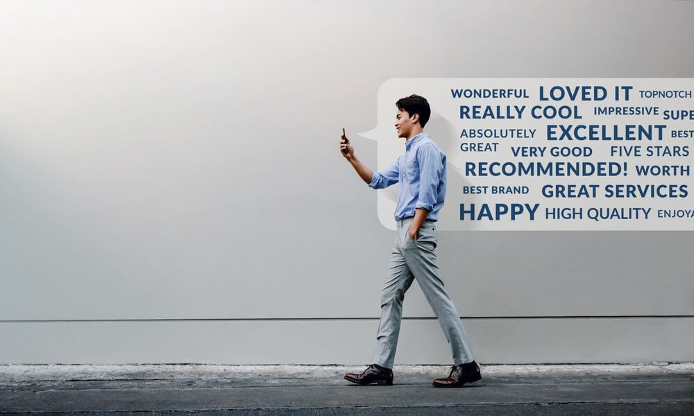 feedback_Customer Experience Concept. Reading Positive Online Review via Smartphone. Smiling Young Businessman Using Mobile Phone while Walking by the Urban Building Wall. Side View. Full Length