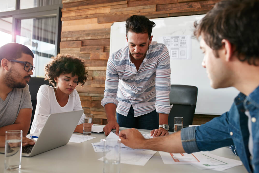 business agency_Young man discussing market research with colleagues in a meeting. Team of young professionals having a meeting in conference room looking at documents