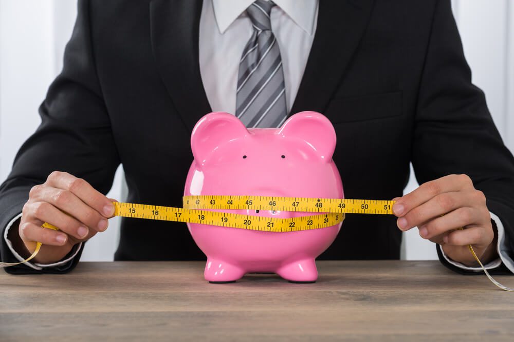 tight budget_Close-up Of Businessman Measuring Piggybank With Measure Tape At Wooden Desk
