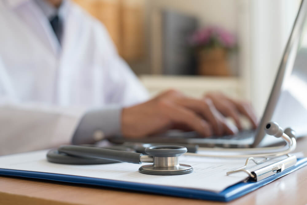 medical search_Doctor working on laptop computer and medical stethoscope on clipboard on desk, telemedicine or teleconference, electronics health record system EHRs, electronics medical record system EMRs concept.