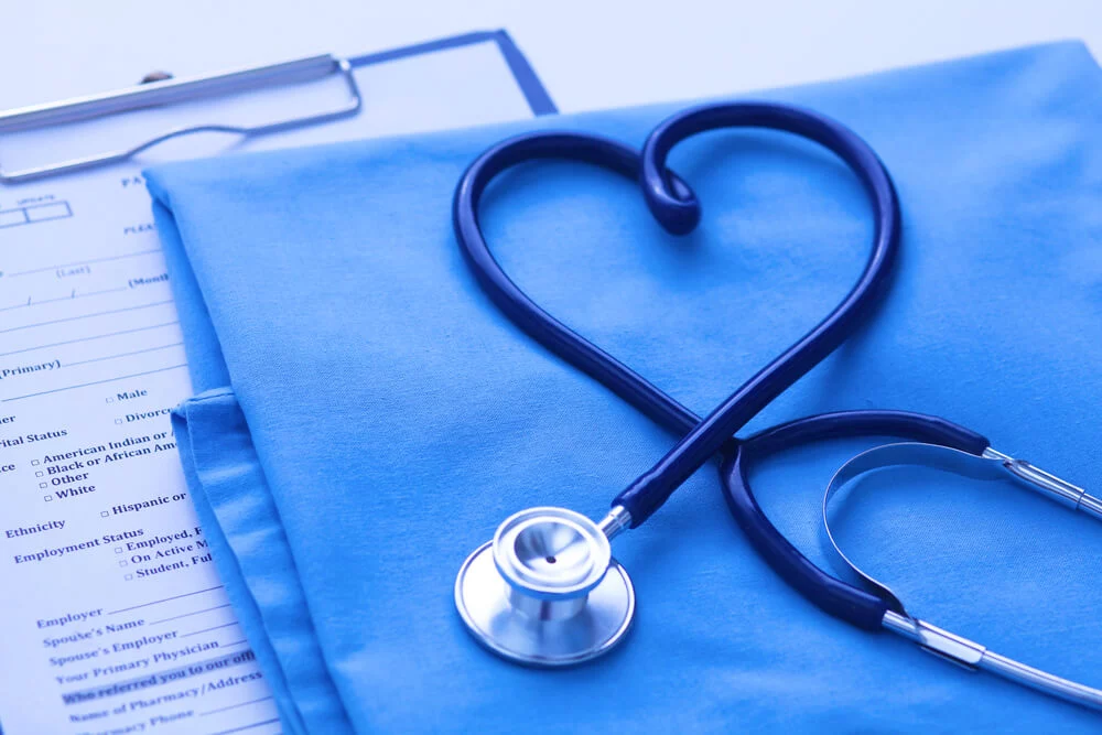 medical_Medical stethoscope twisted in heart shape lying on patient medical history list and blue doctor uniform closeup. Medical help or insurance concept. Cardiology care, health, protection and prevention