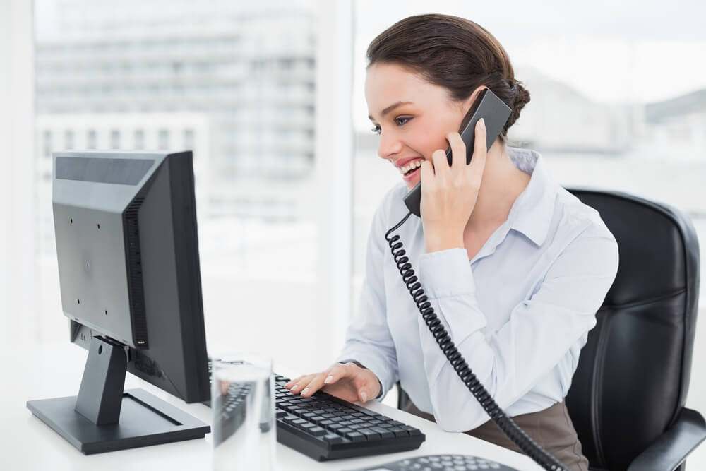 call a business_Smiling elegant businesswoman using landline phone and computer in a bright office