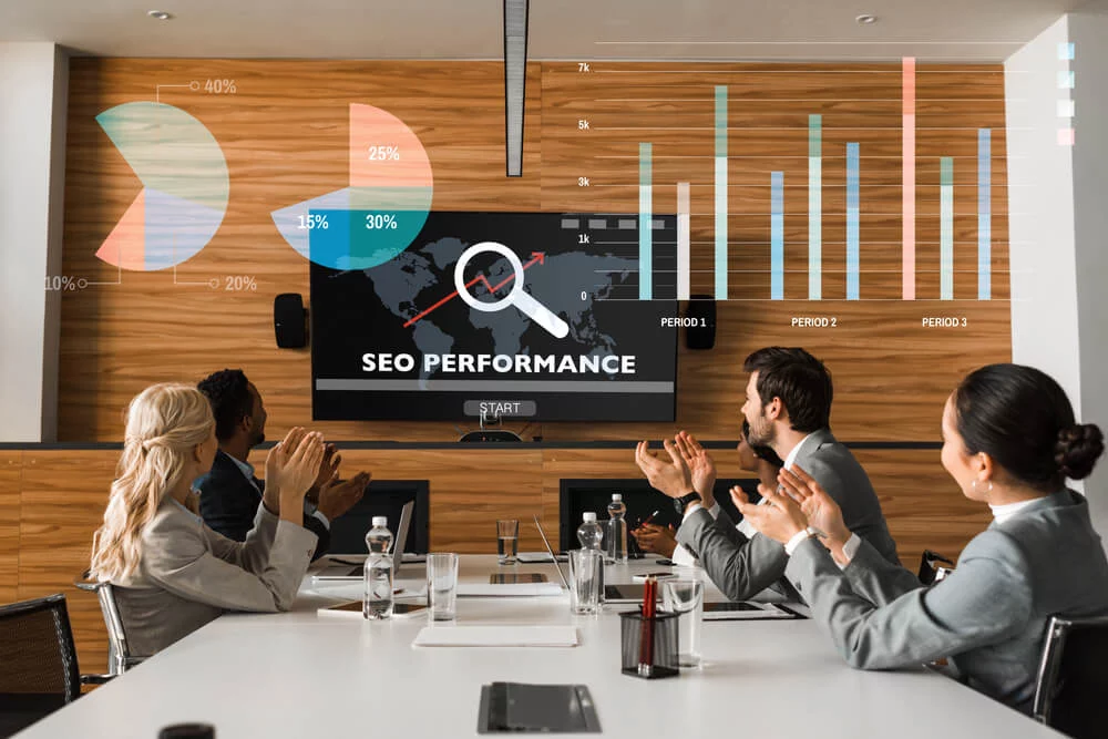 seo team_young multicultural businesspeople applauding while sitting in conference hall and looking at lcd screen on wall, seo performance illustration