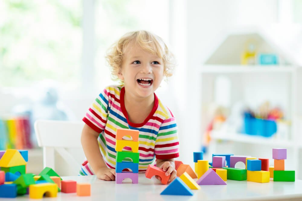 daycare_Kid playing with colorful toy blocks. Little boy building tower of block toys. Educational and creative toys and games for young children. Baby in white bedroom with rainbow bricks. Child at home.