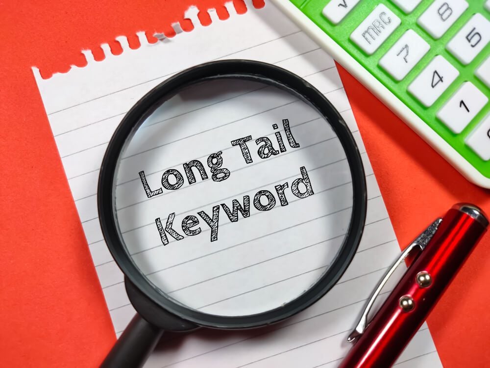 long-tail keywords_Business concept.Text Long Tail Keyword writing on notepaper with magnifying glass,calculator and pen on a red background.