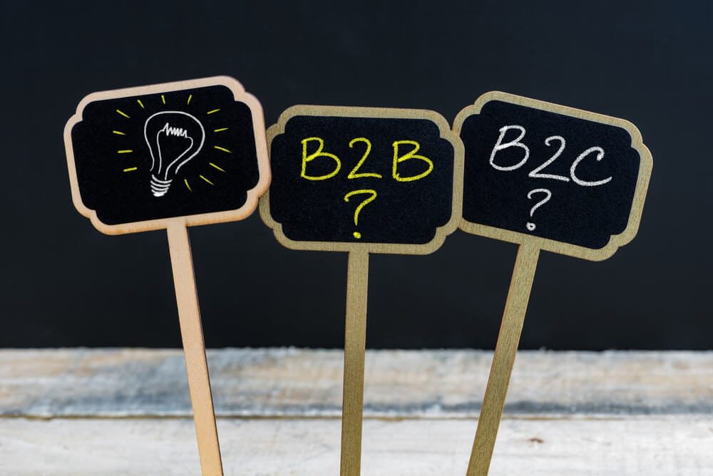 B2B B2C_Concept message B2B as Business To Business, B2C as Business To Consumer and light bulb as symbol for idea written with chalk on wooden mini blackboard labels, chalkboard and wood table in background