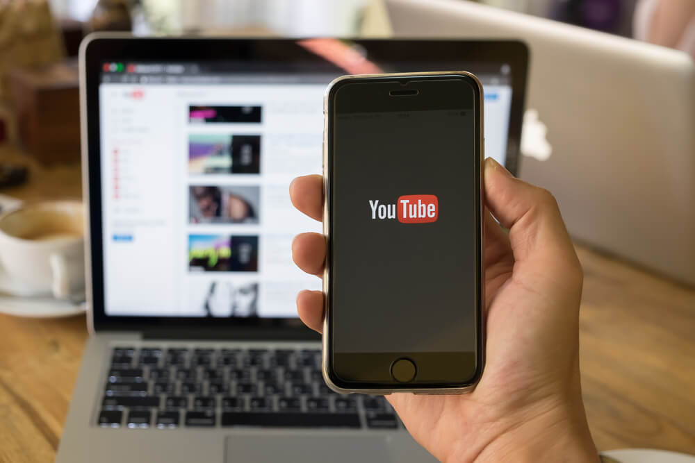 youtube_CHIANG MAI,THAILAND - JAN 26, 2017: A woman showing screen shot of Youtube on iphone 6s. YouTube app on the screen lying on old wood desk. YouTube is the popular online video sharing website.