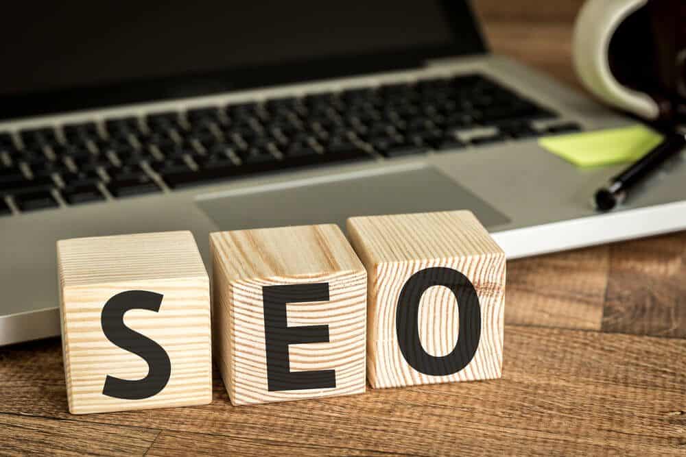 facebook seo_SEO (Search Engine Optimization) written on a wooden cube in front of a laptop