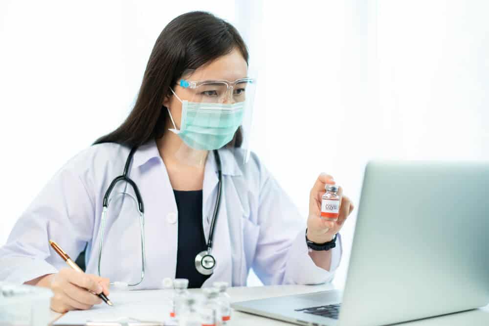 healthcare_Asian female doctor reporting a diagnostic result of Coronavirus or COVID-19 vaccine usage in patient, 2019-nCoV COVID19 cases statistic. Woman analyst - researcher making a video conference.