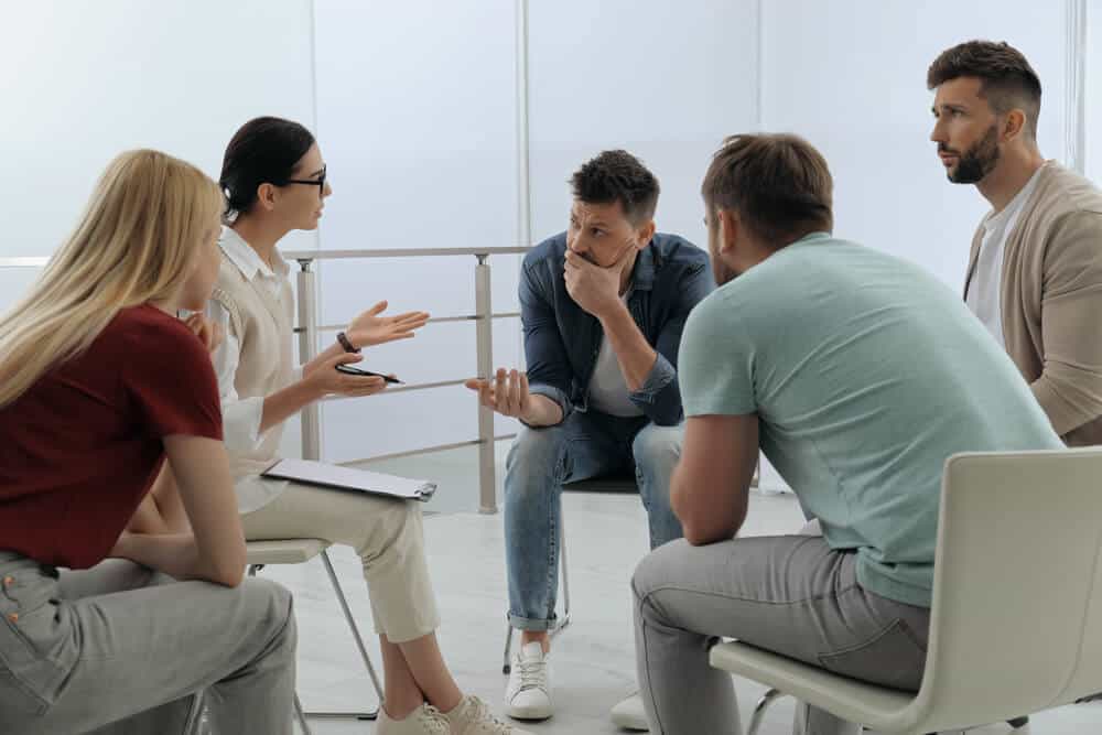 drug rehab_Psychotherapist working with group of drug addicted people at therapy session indoors