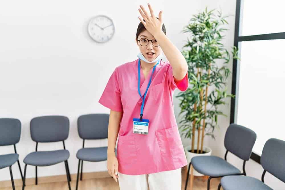 patient forget appointment_Young asian nurse woman at medical waiting room surprised with hand on head for mistake, remember error. forgot, bad memory concept.