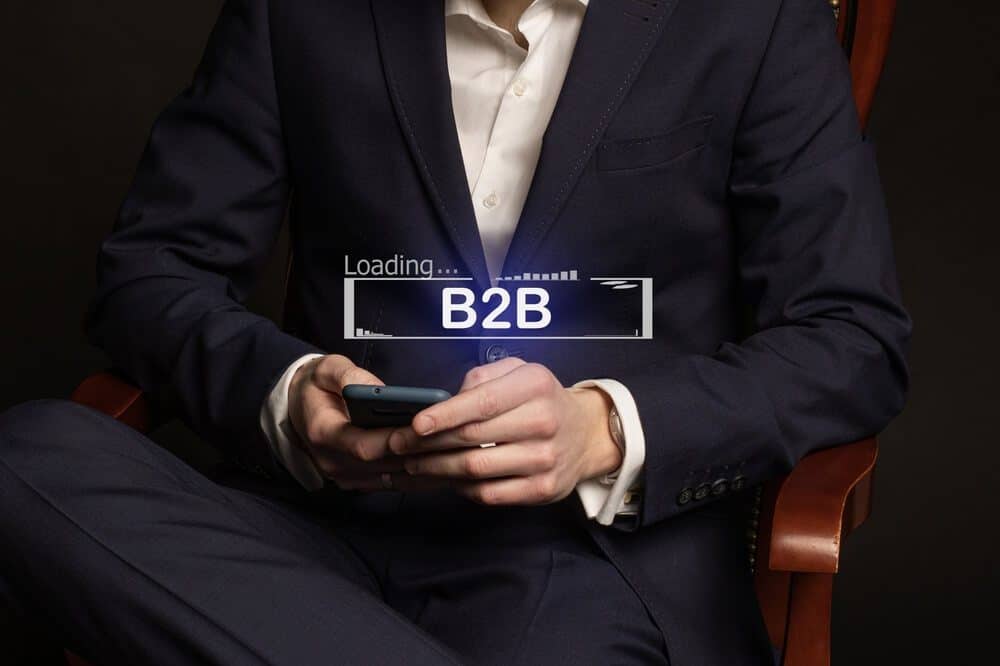 B2B_Office manager in a suit at the workplace and the inscription B2B on the display of his phone, B2B e-commerce market, business strategy search