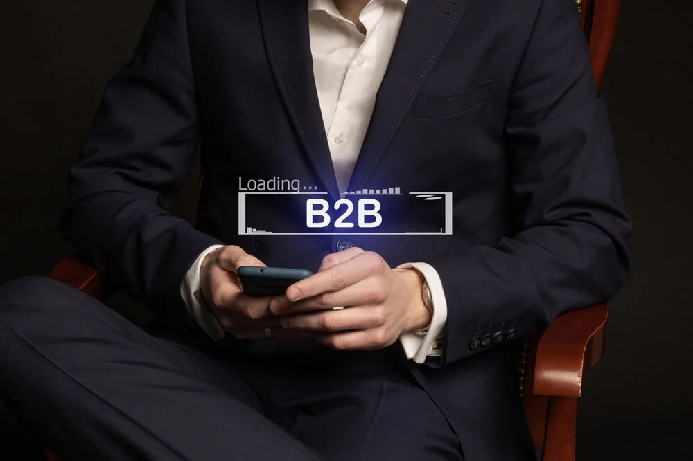 B2B_Office manager in a suit at the workplace and the inscription B2B on the display of his phone, B2B e-commerce market, business strategy search
