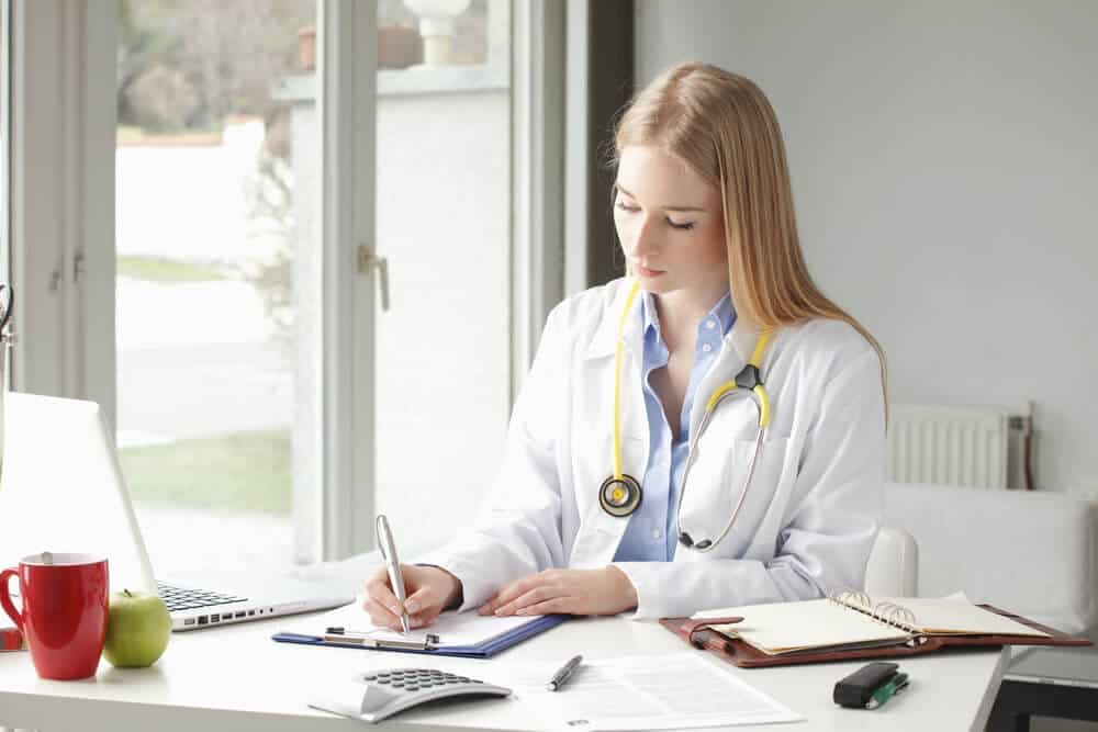 healthcare content_Female doctor sitting and writing at desk in clinic.