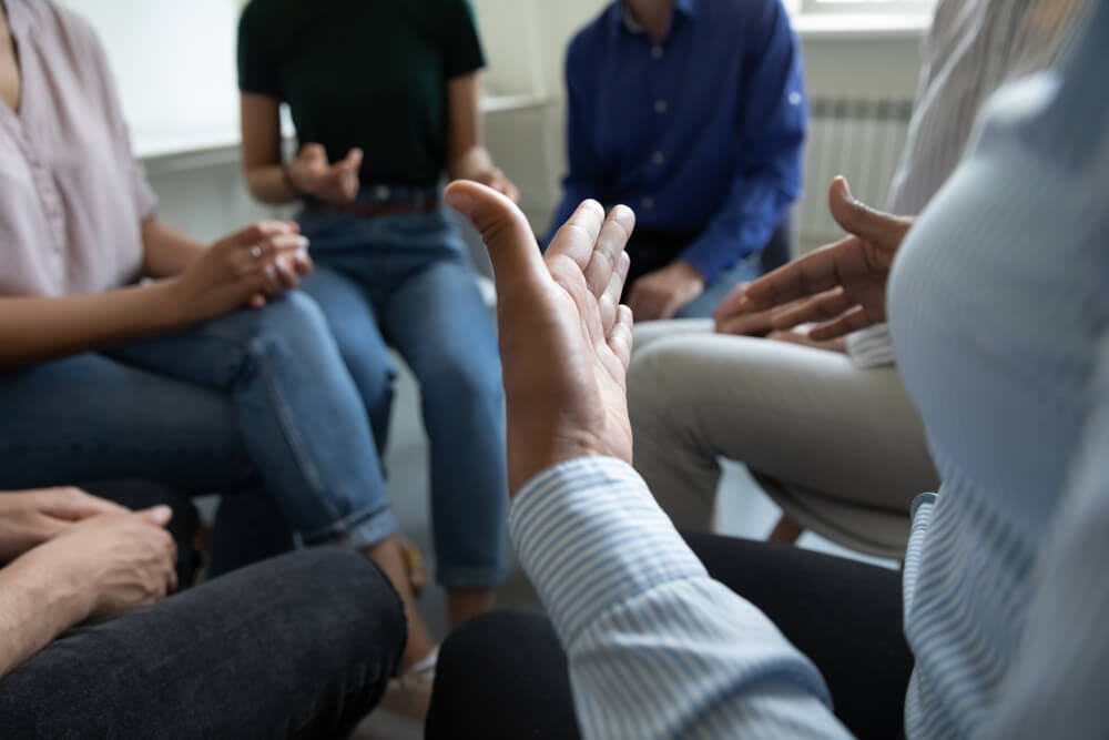 drug rehab marketing_Sharing ideas. Close up view of diverse people group gathered in circle at workplace office cabinet to discuss work or self problems, share points of view, listen to mates, feel psychological support