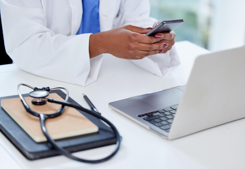 hospital content_A doctor whos always busy. Shot of an unrecognizable doctor using a phone and laptop at work.