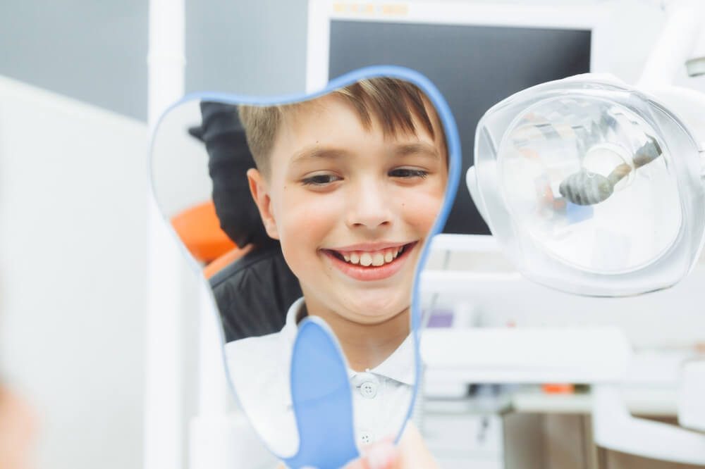 dentist content_boy looks in the mirror with a toothy smile, sitting on a chair with a dentist in the dental office.