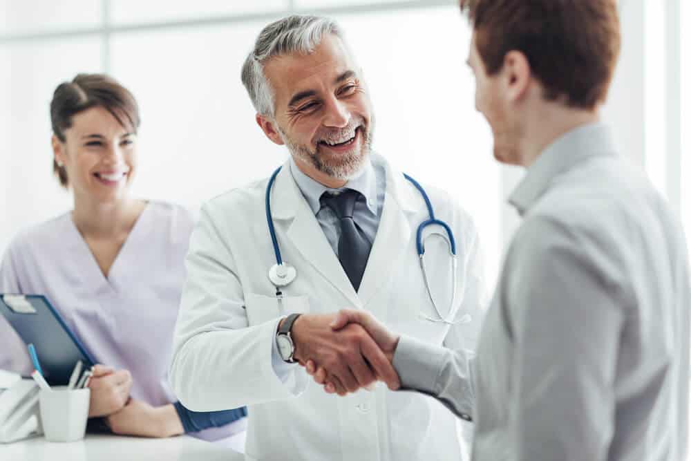 healthcare patients_Smiling doctor at the clinic giving an handshake to his patient, healthcare and professionalism concept