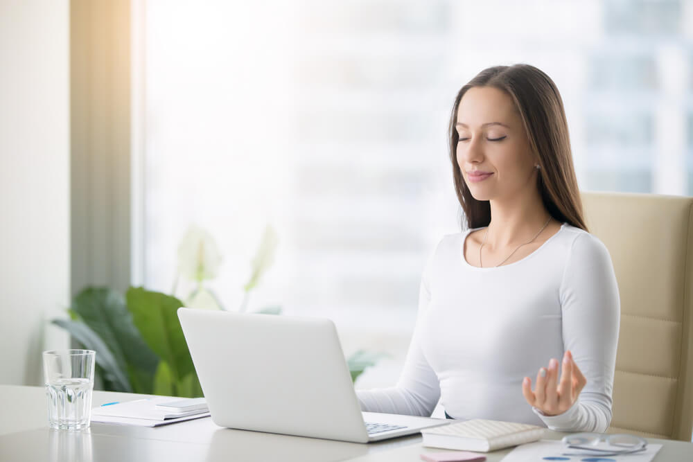 fitness company_Young woman near the laptop, practicing meditation at the office desk, in front of laptop, online yoga classes, taking a break time for a minute, healing from paperwork and laptop radiation