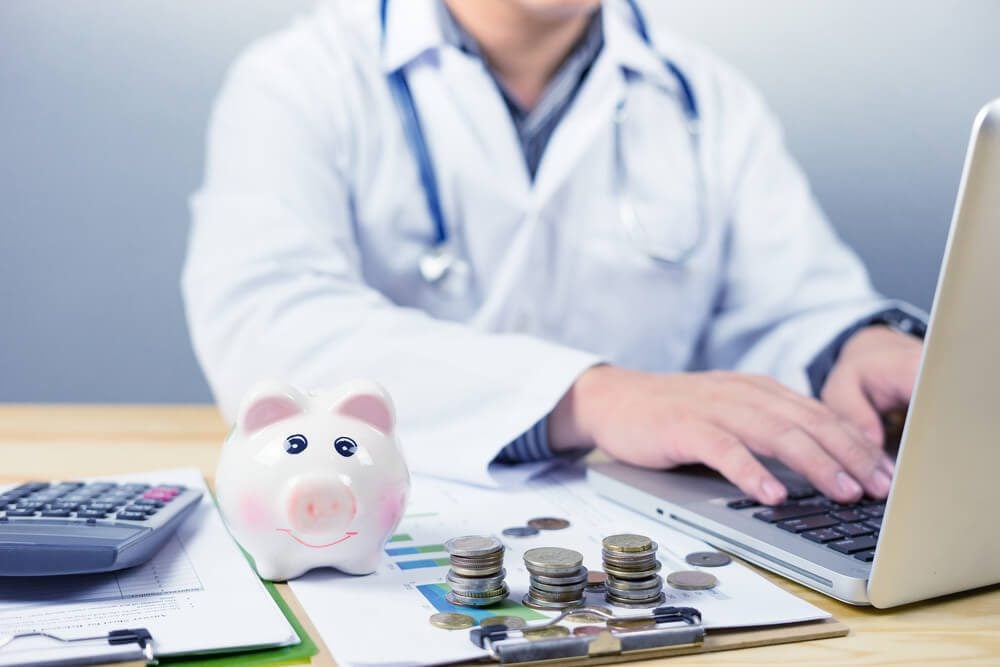 hospital revenue_young medical doctor caucasian healthcare professional wearing a white coat with stethoscope in hospital,calculates on an electronic calculator laptop,medical fee concept,selective focus,vintage color