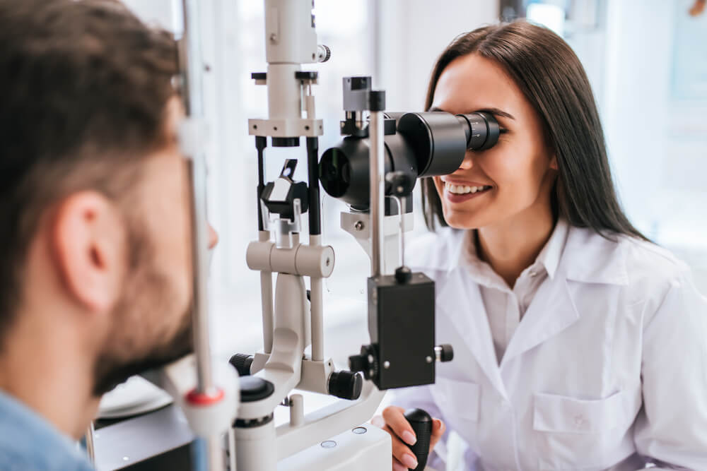 optometry_Attractive female doctor ophthalmologist is checking the eye vision of handsome young man in modern clinic. Doctor and patient in ophthalmology clinic.