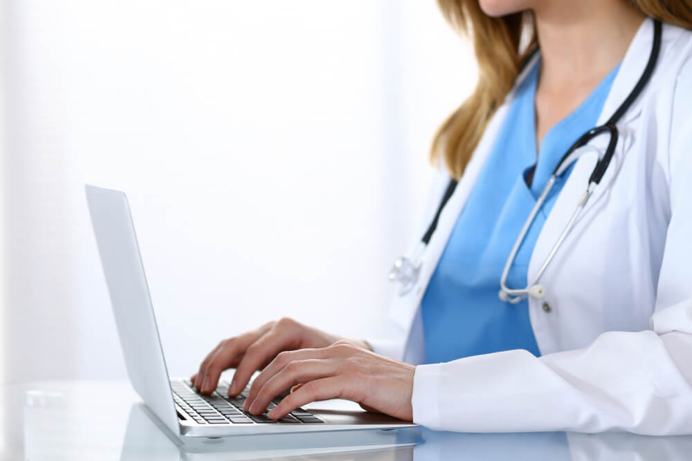 healthcare email_Doctor typing on laptop computer while sitting at the glass desk in hospital office. Physician at work. Medicine and healthcare concept